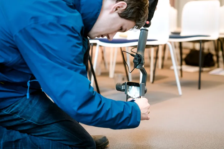 Teilnehmer kniet mit einem Smartphone-Gimbal am Boden und übt Videoaufnahmen