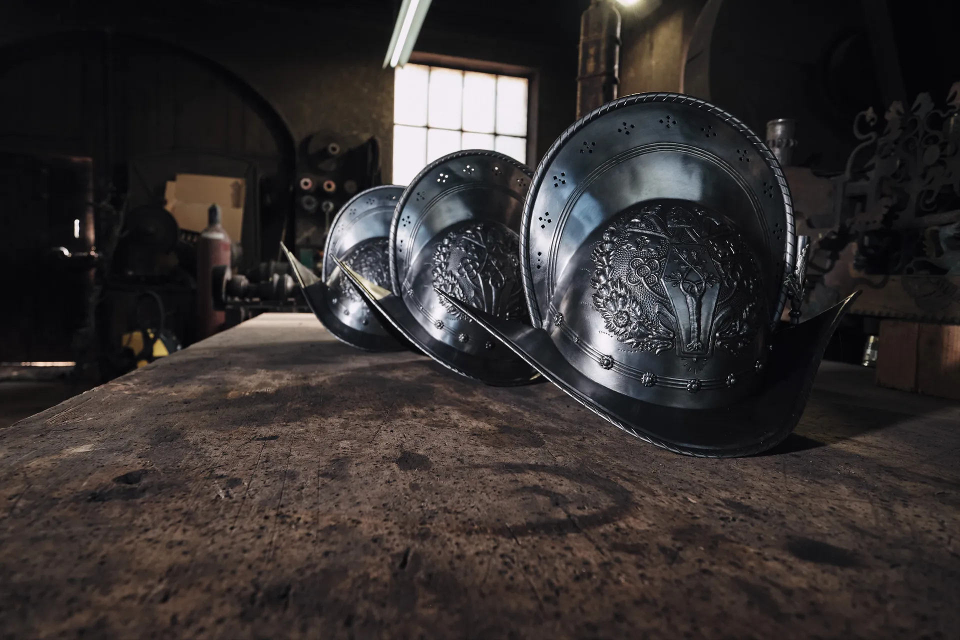 Drei fertige Helme im Stil der Päpstlichen Schweizergarde stehen im Gegenlicht auf der Werkbank.