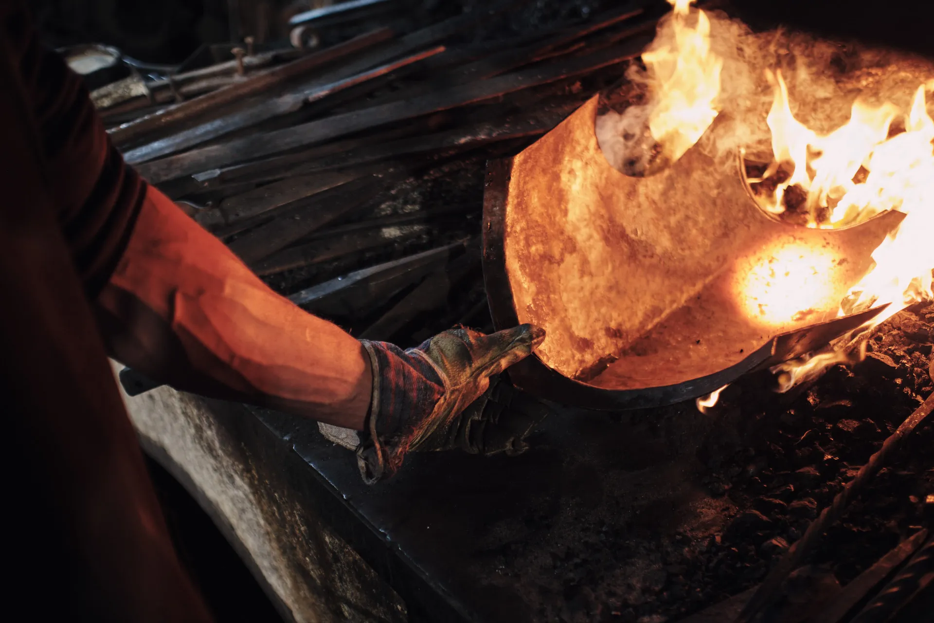 Mit dickem Lederhandschuh zieht ein Schmied den rotglühenden Helmrohling aus dem Feuer.