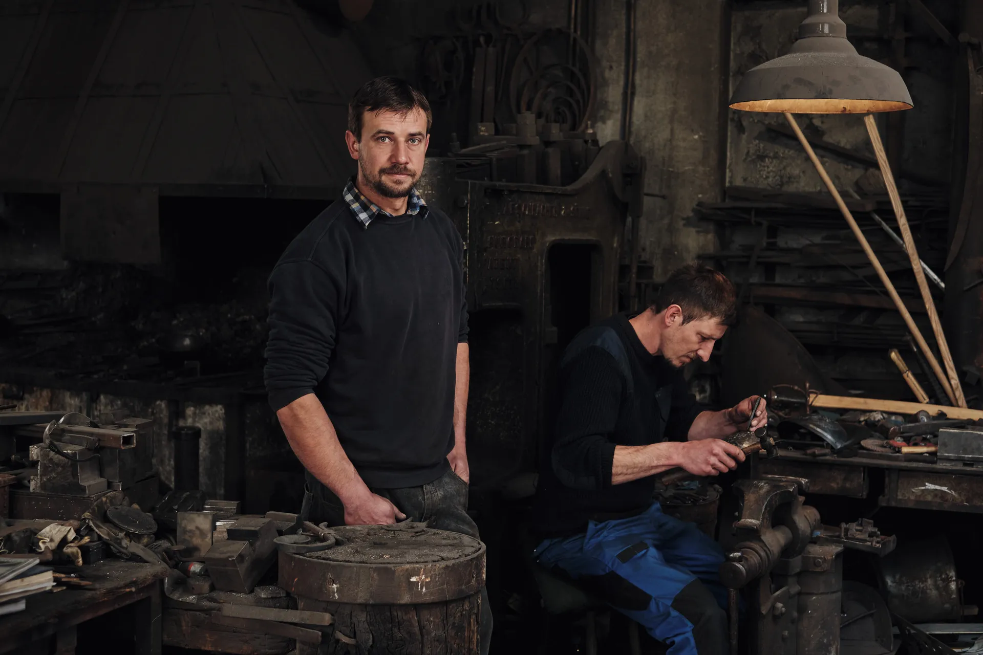 Georg Schmidberger blickt in die Kamera, im Hintergrund arbeitet sein Bruder Hans an einem Helm, Werkstatt Schmidberger in Molln.